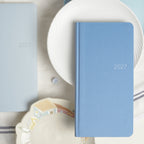 Blue CRENA 2027 weekly planner displayed against white tableware
