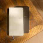 Cream and dark textured CRENA 2027 weekly planners on a wooden surface