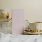 Pale pink CRENA 2027 weekly planner displayed beside teacups