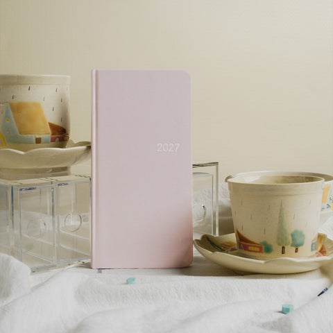 Pale pink CRENA 2027 weekly planner displayed beside teacups